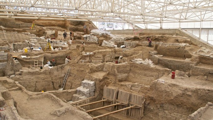 Many unearthed partial structures dot a large dig site protected by a modern roof