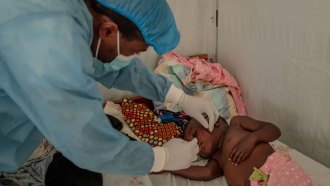 A health care worker wearing medical protective gear checks on a young boy at an mpox treatment center.