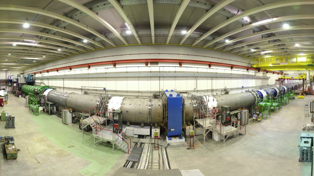 A long, cylindrical particle physics experiment is show in a wide-angle image.